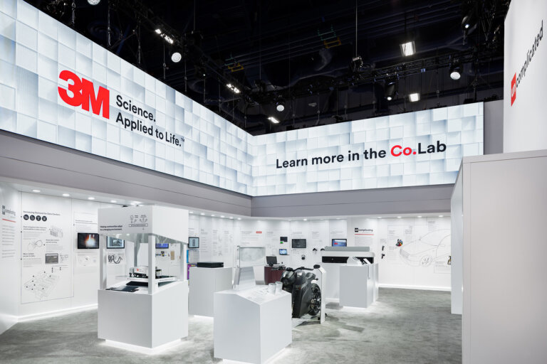 Image of the 3M booth at CES 2025, which features an LED screen banner around the top of the walls, and a variety of display cases with 3M products below