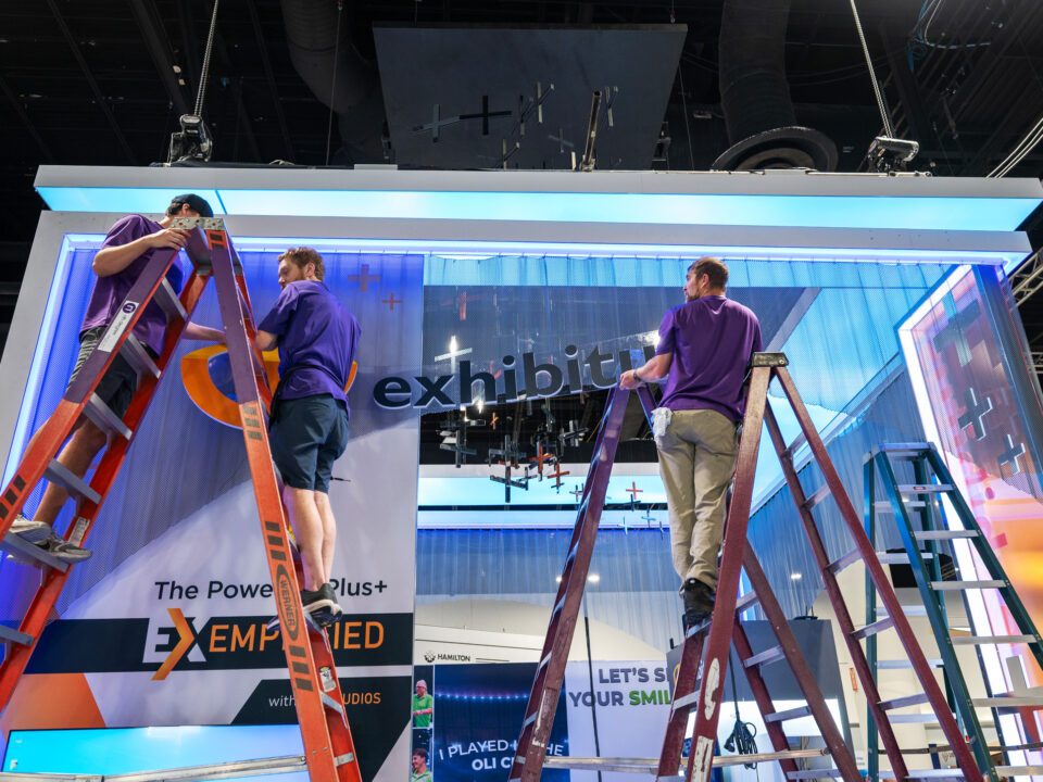 A STAR installation team works together to suspend layered graphics and signage on a 30' exhibit.